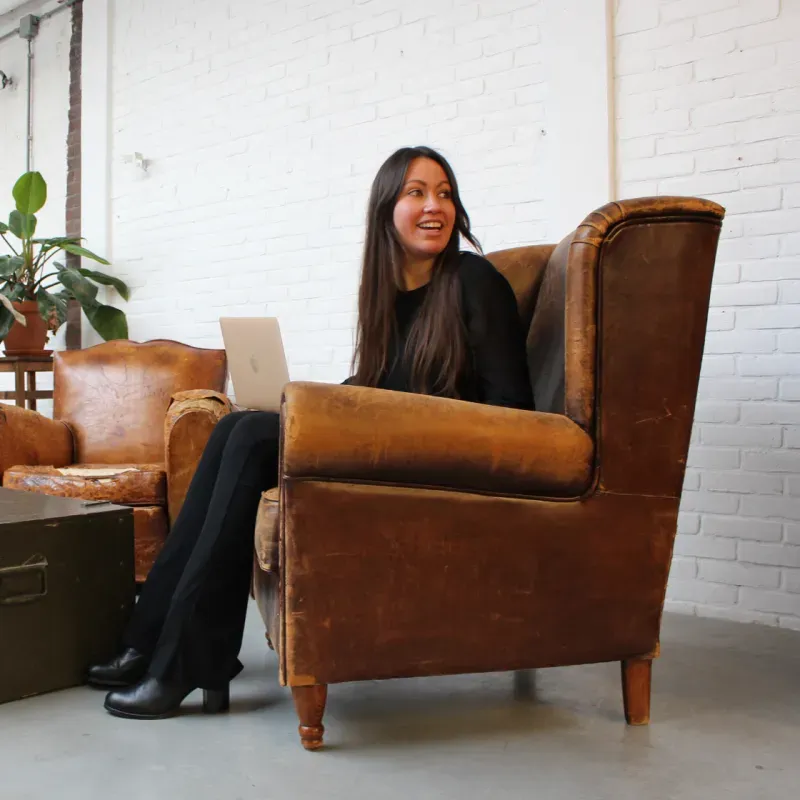 Lisa van der Lee, oprichter van SUSJOYA, met haar laptop in een leren fauteuil